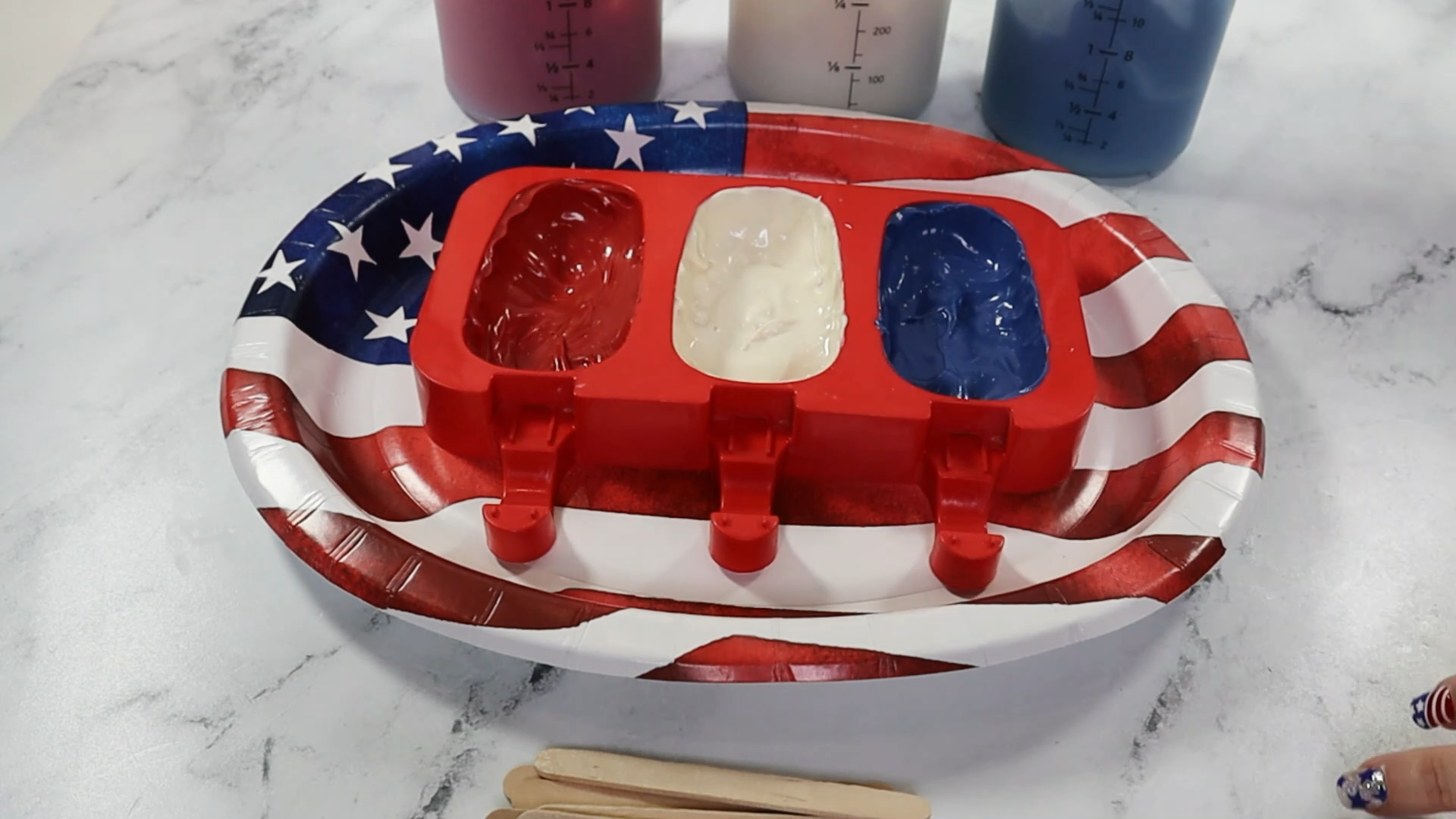 begin to make fourth of july cakesicles by coating the bottom of the silicone popsicle mold with chocolate in red white and blue